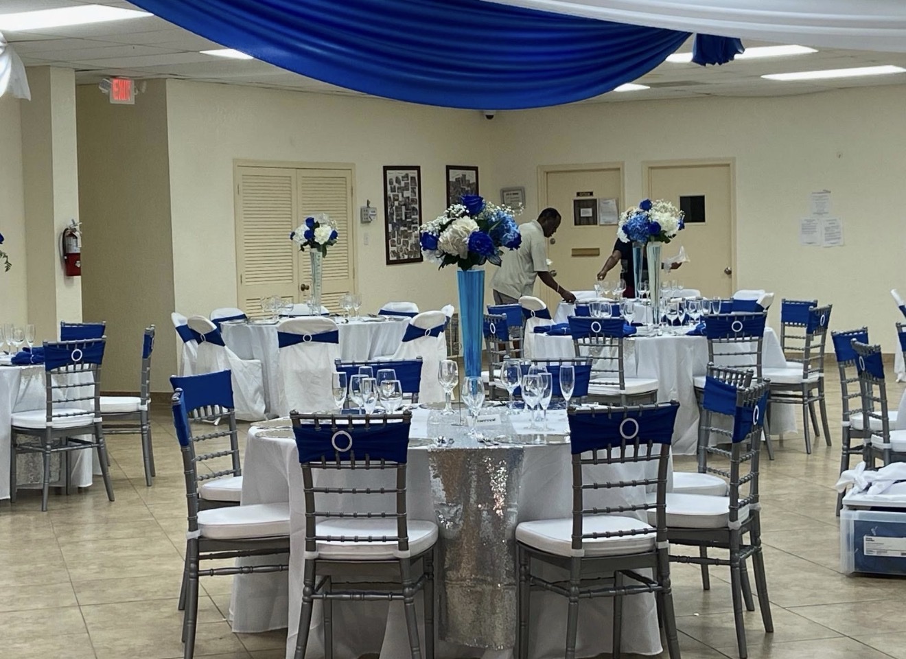 Reception hall with blue and white floral centerpieces and chiavari chairs with blue sashes