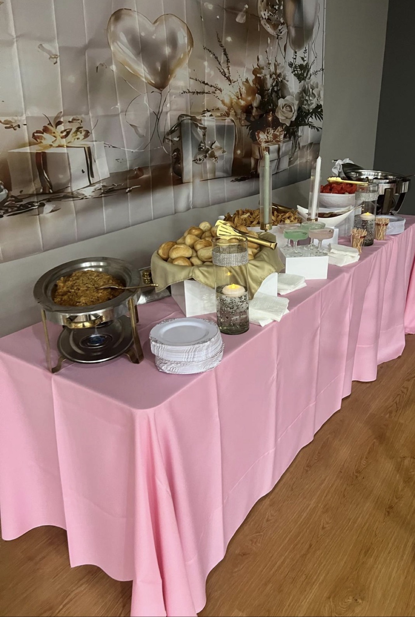 Pink buffet table with chafing dishes, dinner rolls, and plates