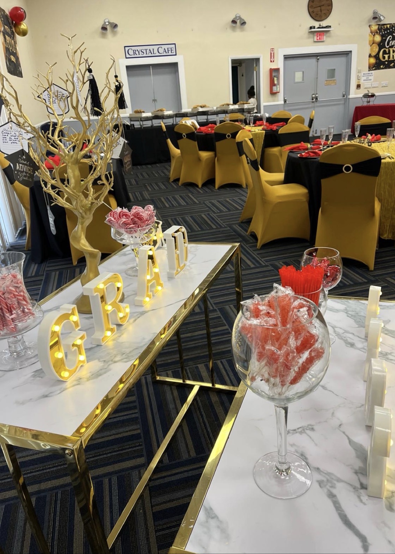Graduation party setup with lit GRAD letters, a candy table and black and gold chairs