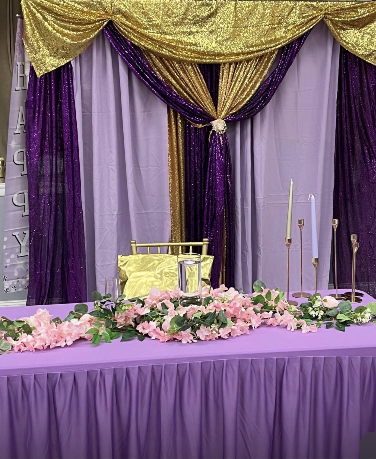 Head table with a pink floral garland before a purple and gold drapery backdrop
