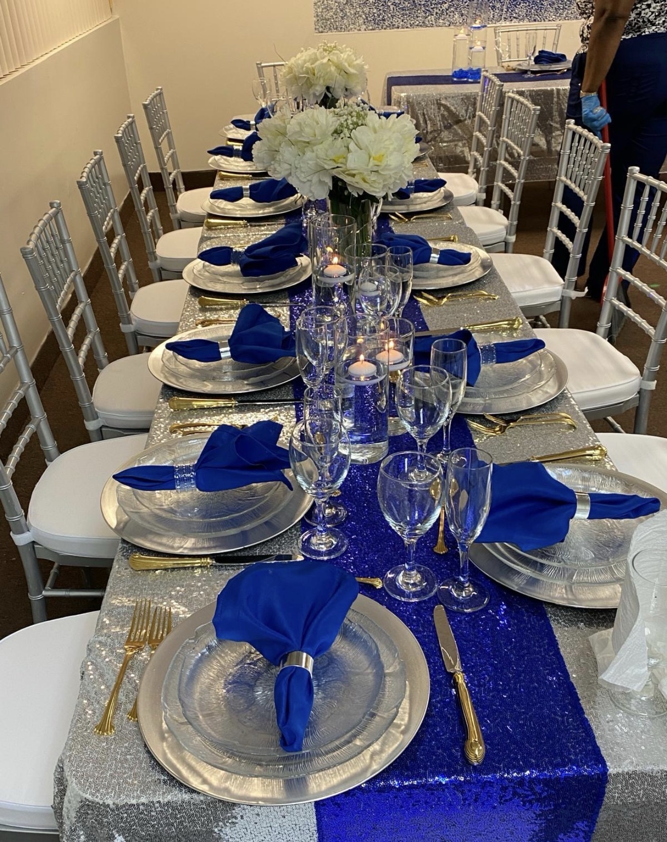 Long banquet table with royal blue napkins, silver sequin cloth and gold flatware