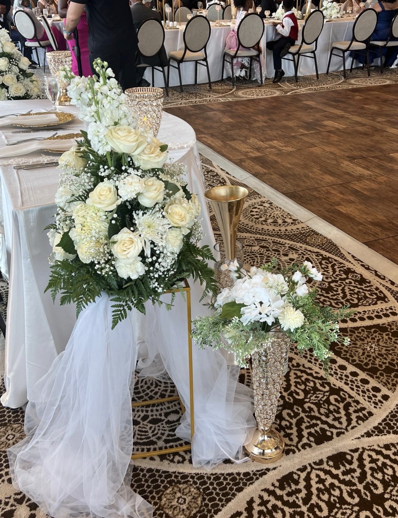 Elegant head table with white rose floral arrangements and crystal and gold vases